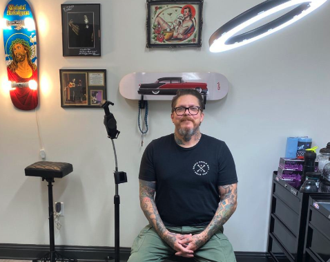 Jason “Elvis” Martin pictured inside his private Hendersonville studio, surrounded by artwork and tattoo equipment.